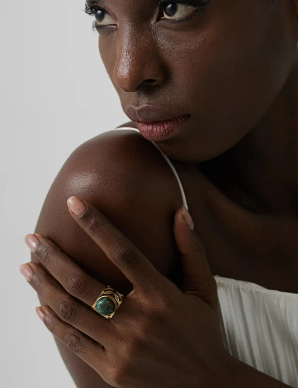 A woman in a white spaghetti strap top looks to the side, resting her hand on her shoulder and wearing the Turquoise Statement Ring, which adds a touch of bohemian jewelry flair.