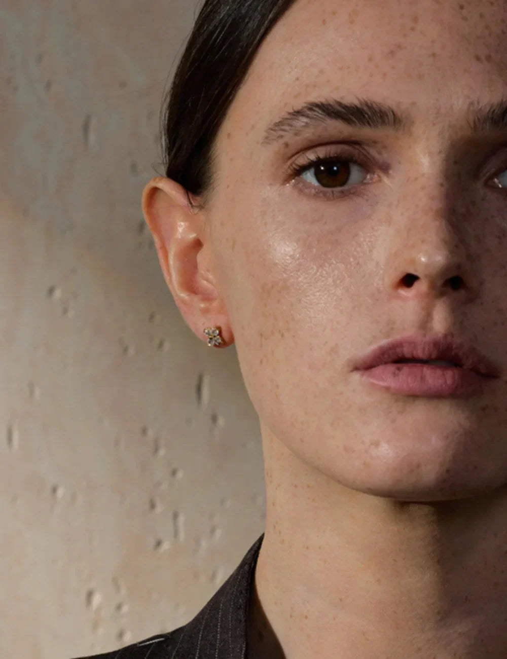 Close-up of a woman wearing small gold stud earrings with crystal details, minimalist jewelry photography