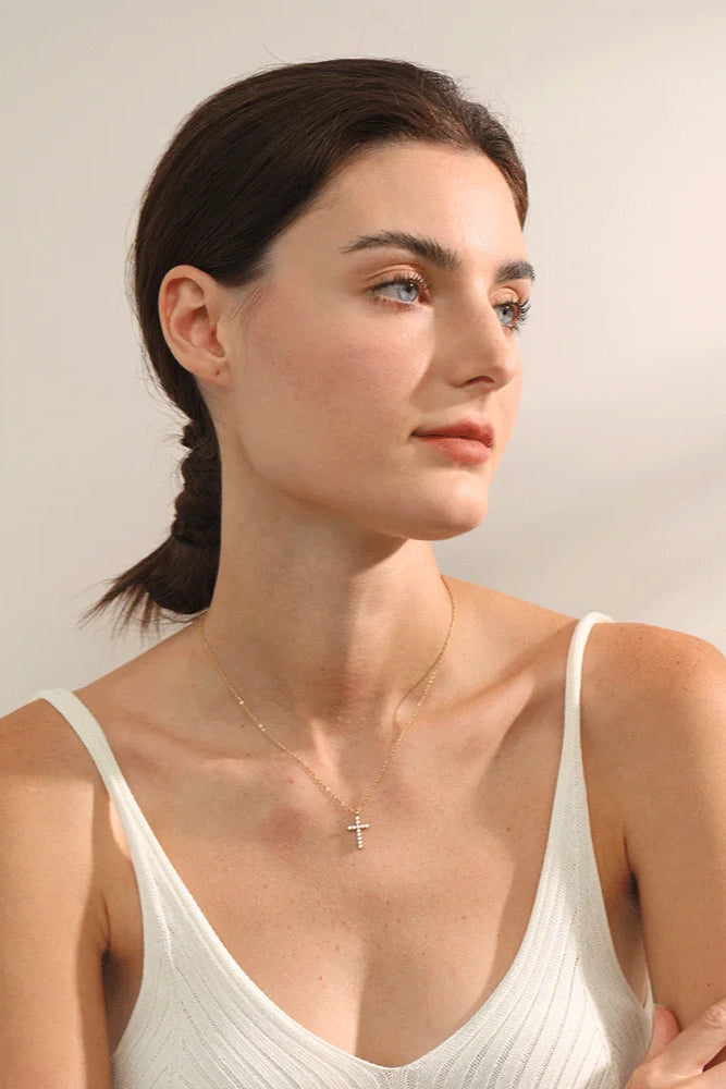 Woman wearing a minimalist gold cross necklace with a white top, elegant jewelry photography