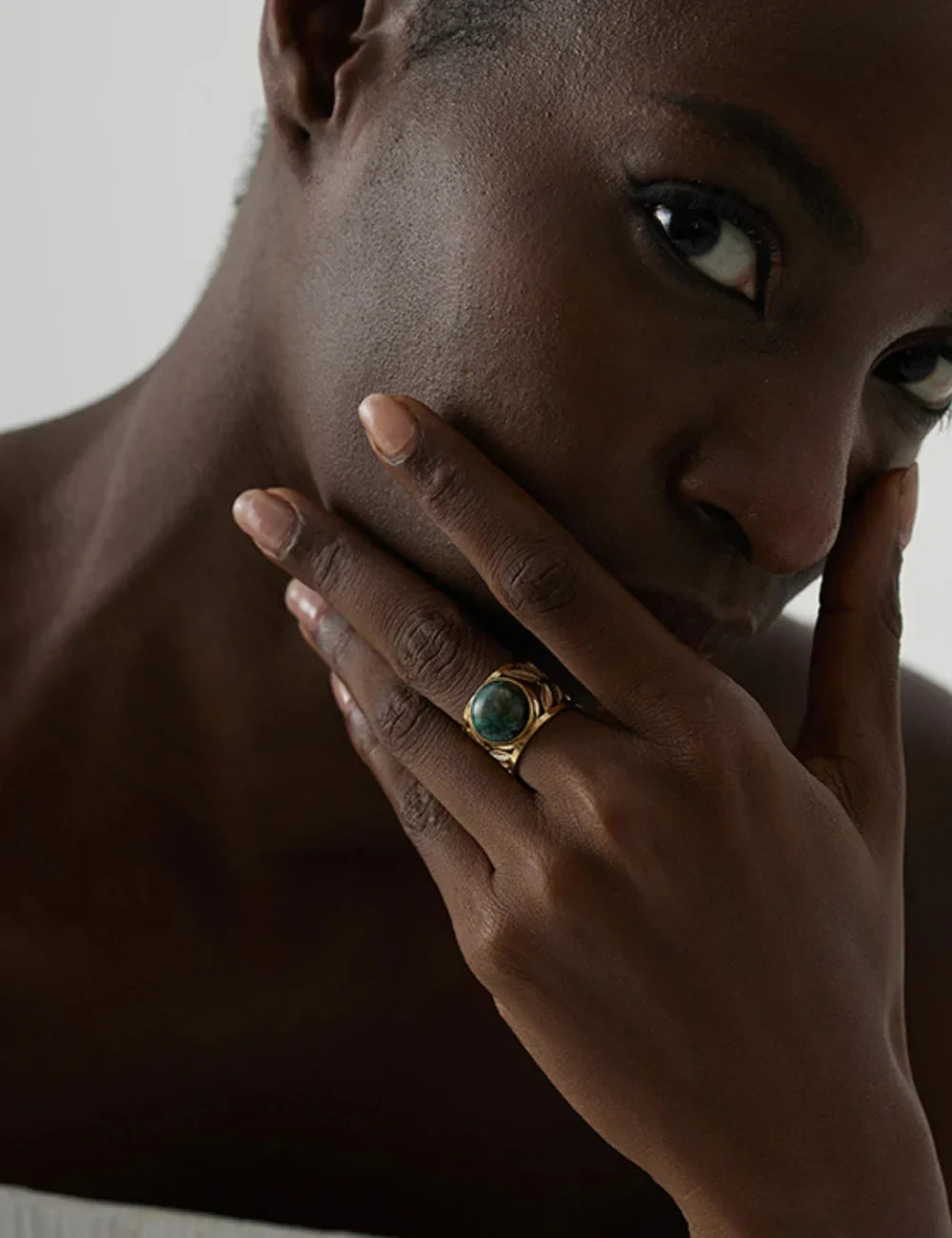 Close-up of a woman wearing a bold gold ring with green gemstone, elegant jewelry photography
