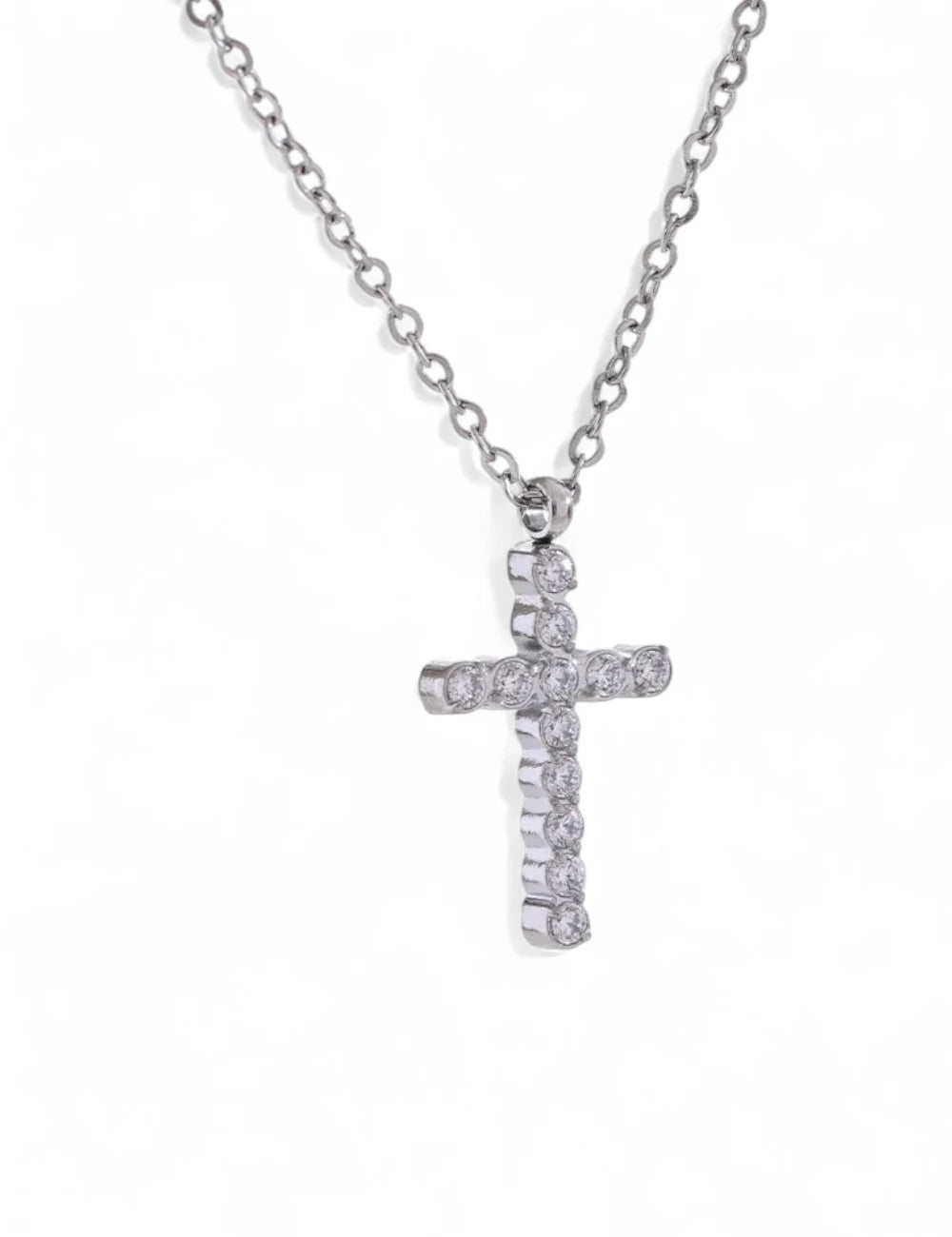 The Grace Cross Pendant Necklace features a silver cross adorned with round, clear cubic zirconia gemstones, elegantly displayed against a white background.
